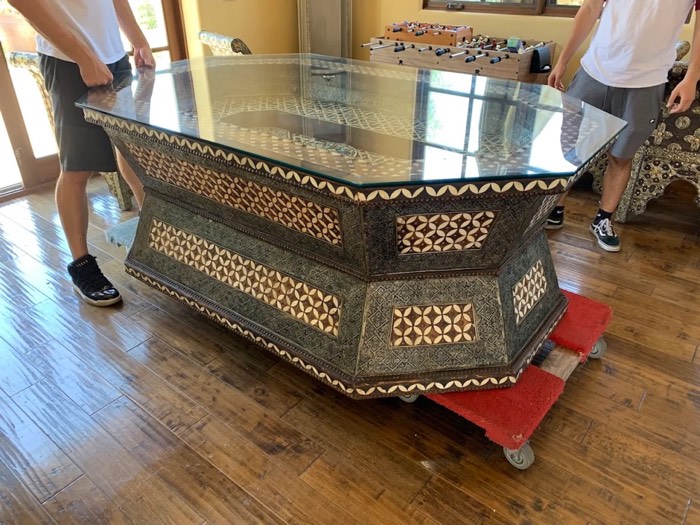 Happy Home Movers crew moving a large ornate glass-top table with a furniture dolly